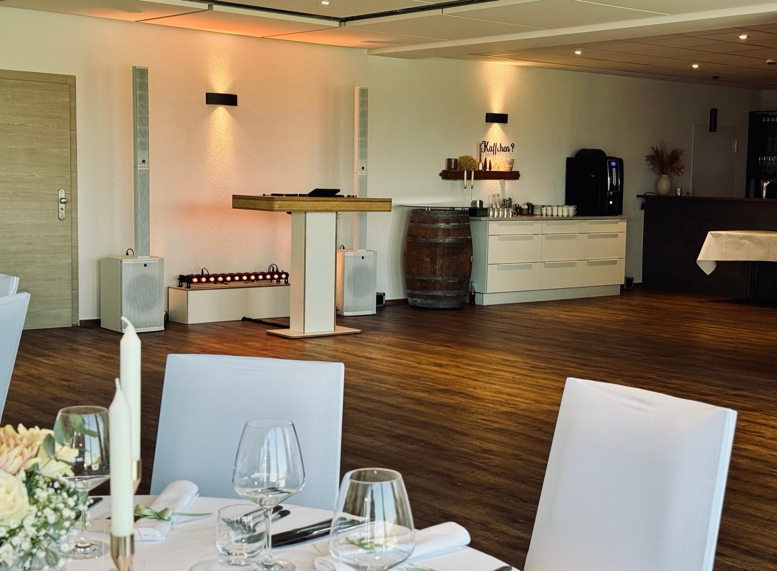 DJ booth in white and wood with white column speakers, seen across a table set for a wedding dinner