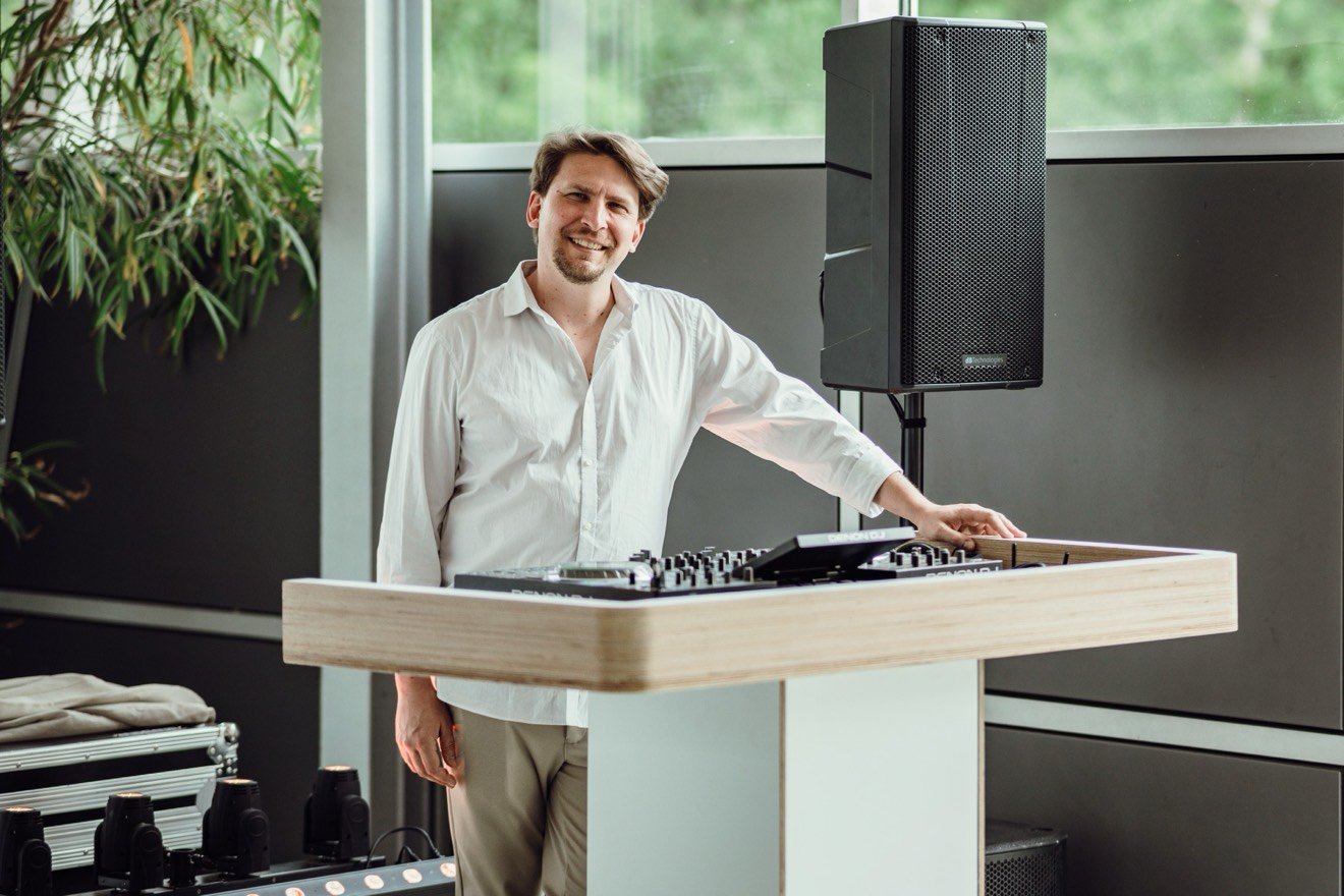 Felix Krüger lächelnd an seinem DJ-Tisch in Weiß und Holz