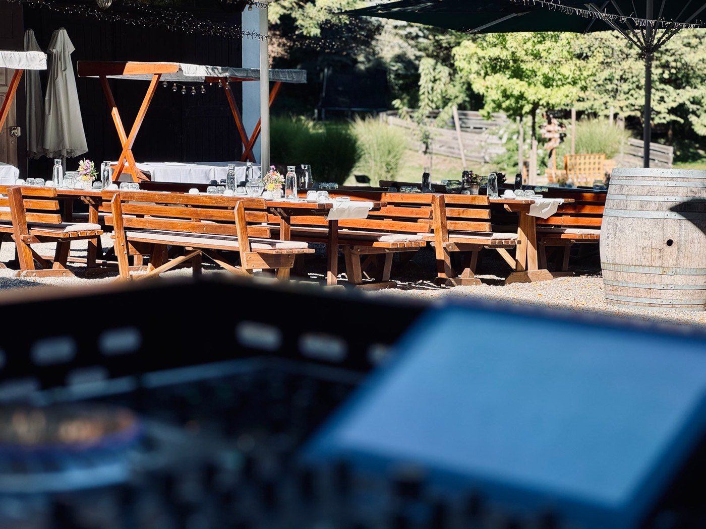 Blick über das DJ-Pult in den Innenhof des Hofguts Lilienhof mit Holztischen und Bänken